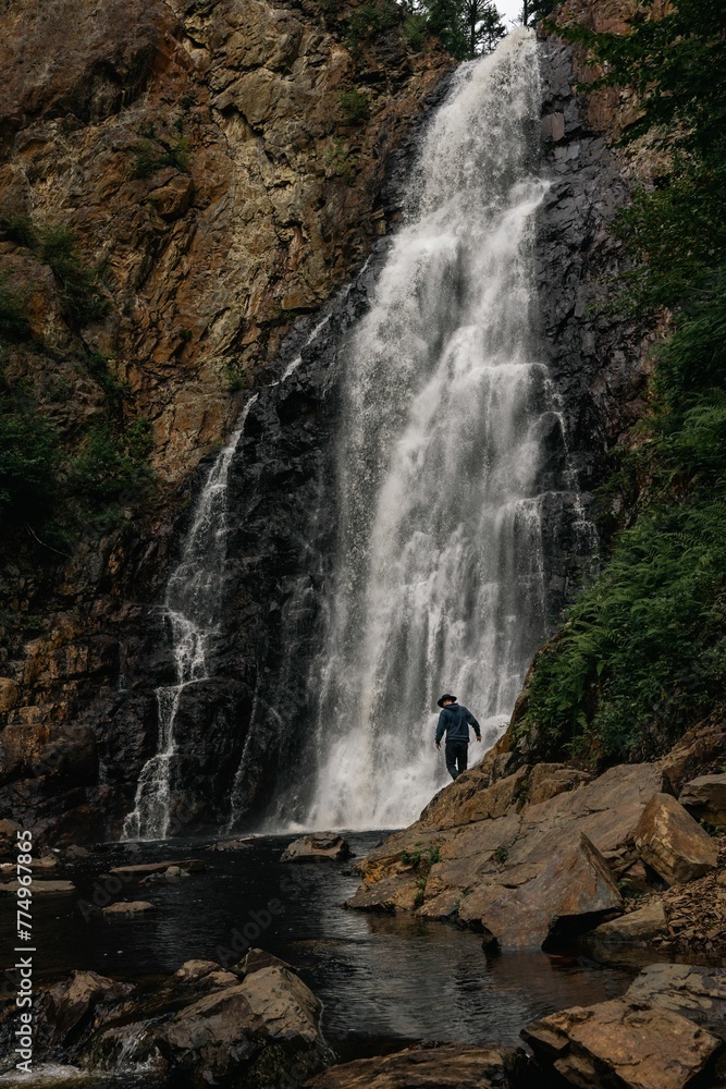 Vertical shot of a male tourist walking on rocky cliffs before a scenic waterfall