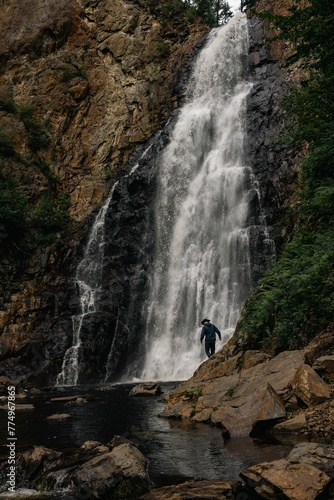 Vertical shot of a male tourist walking on rocky cliffs before a scenic waterfall