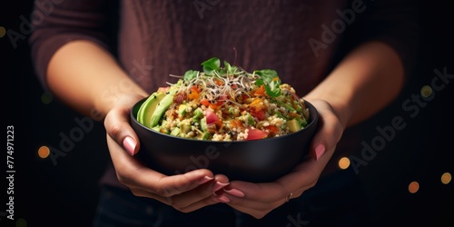 Woman holding bowl of quinoa salad with avocado and sprouts on a dark background