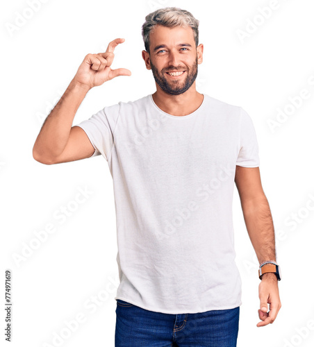 Young handsome blond man wearing casual t-shirt approving doing positive gesture with hand, thumbs up smiling and happy for success. winner gesture.