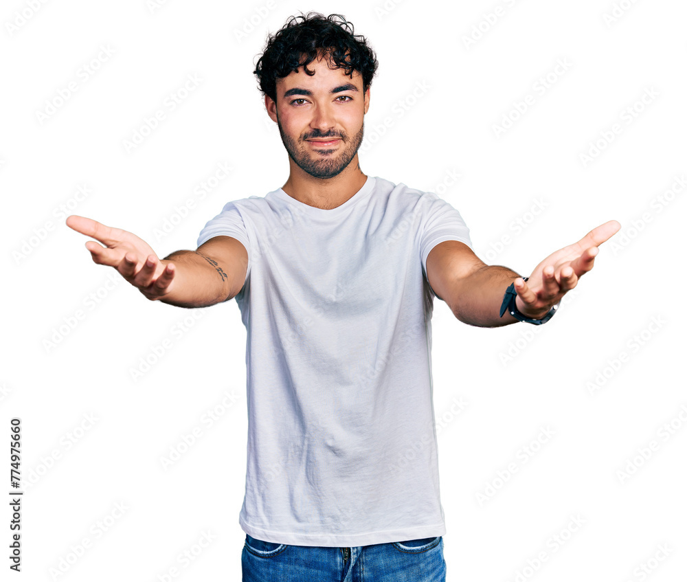 Hispanic young man with beard wearing casual white t shirt smiling cheerful offering hands giving assistance and acceptance. Hispanic young man with beard wearing casual white t shirt smiling cheerful offering hands giving assistance and acceptance.