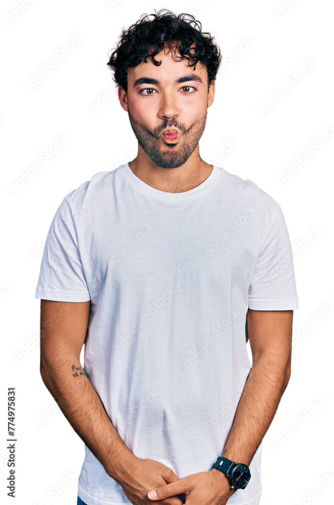 Hispanic young man with beard wearing casual white t shirt making fish face with lips, crazy and comical gesture. funny expression. Hispanic young man with beard wearing casual white t shirt making fish face with lips, crazy and comical gesture. funny expression.