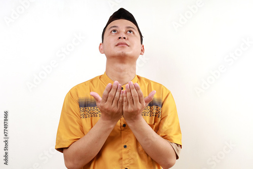 Close up photo of young asian muslim man praying while looking above