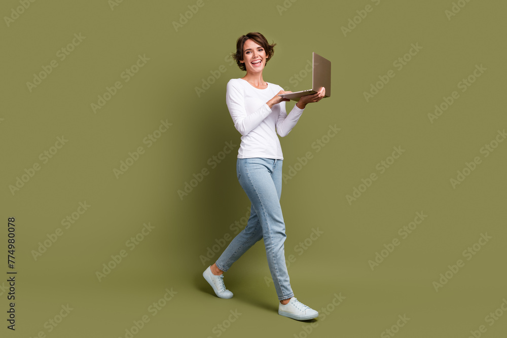 Full body photo of pretty young girl hold netbook walking wear trendy white outfit isolated on khaki color background Full body photo of pretty young girl hold netbook walking wear trendy white outfit isolated on khaki color background