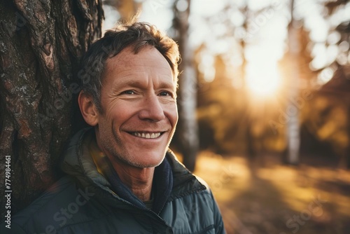 Portrait of a smiling senior man leaning against a tree in the forest photo