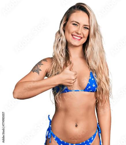 Young blonde woman wearing bikini doing happy thumbs up gesture with hand. approving expression looking at the camera showing success.