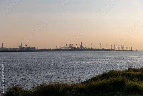 Beautiful windmills in the port of Rotterdam. Beautiful sunset on the sea coast. The Blue North Sea and Water surface. The lighthouse and shore are lit by the sunset sun.