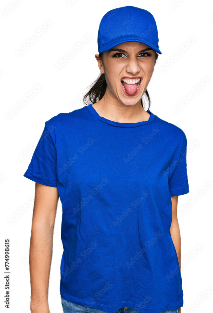 Young hispanic girl wearing delivery courier uniform sticking tongue out happy with funny expression. emotion concept.