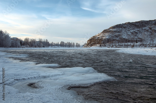 Snowcovered mountain landscape with a frozen river and cloudy sky.