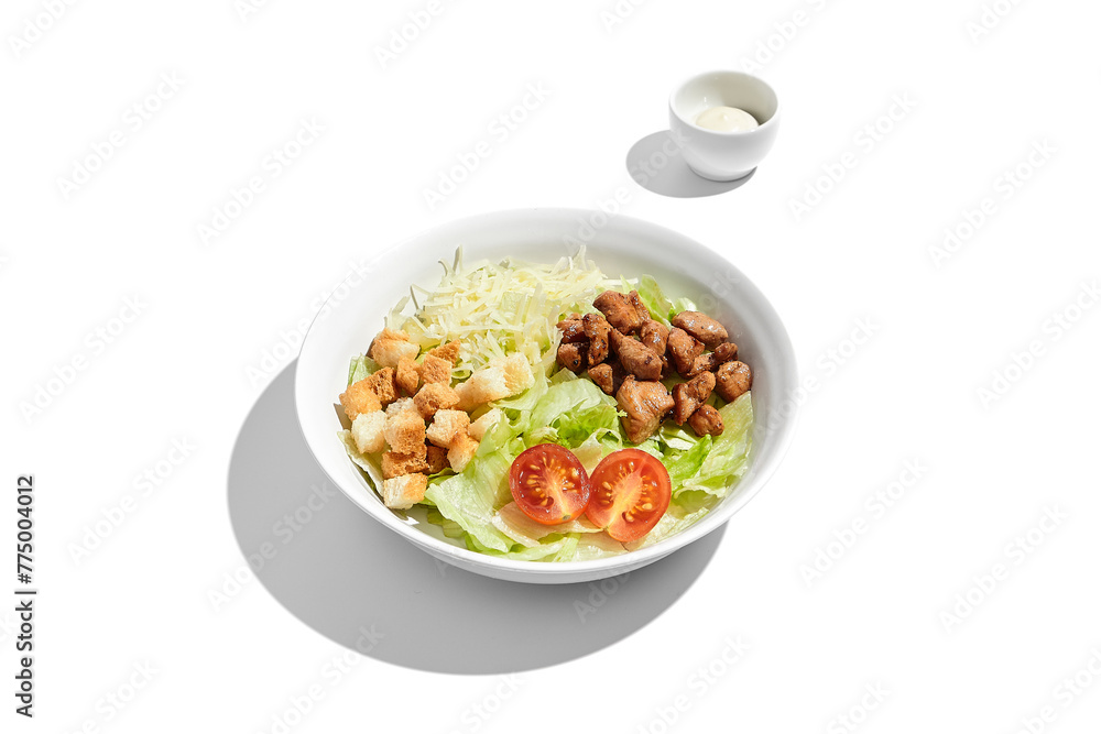 Fresh Caesar salad with crispy croutons and grilled chicken pieces in a white bowl, isolated on a white background with dressing on the side Fresh Caesar salad with crispy croutons and grilled chicken pieces in a white bowl, isolated on a white background with dressing on the side