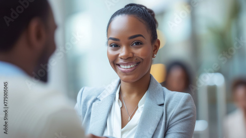 young professional woman is smiling and engaging in a conversation with an out-of-focus male colleague in a bright office environment.