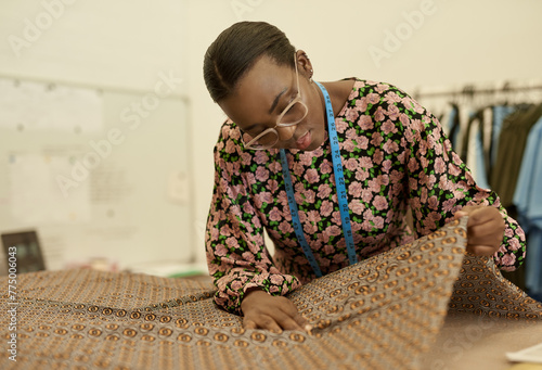 Young African female fashion designer examining some material at a workbench