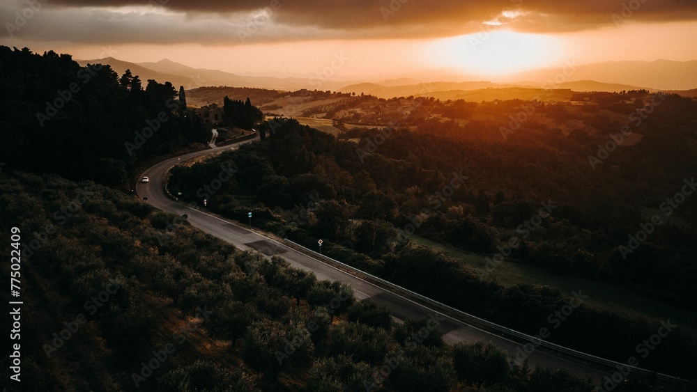 Drone shot over city road with cars and forest trees at sunset with orange sky