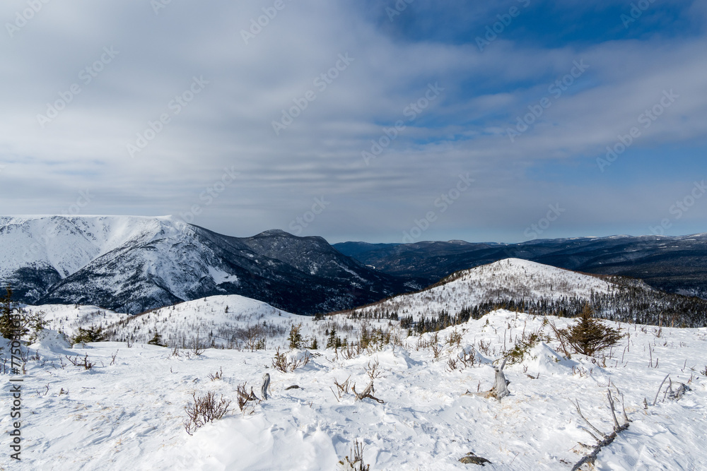 Winter landscape, mountain valley, forest and mountains covered with snow in blue cloudy sky