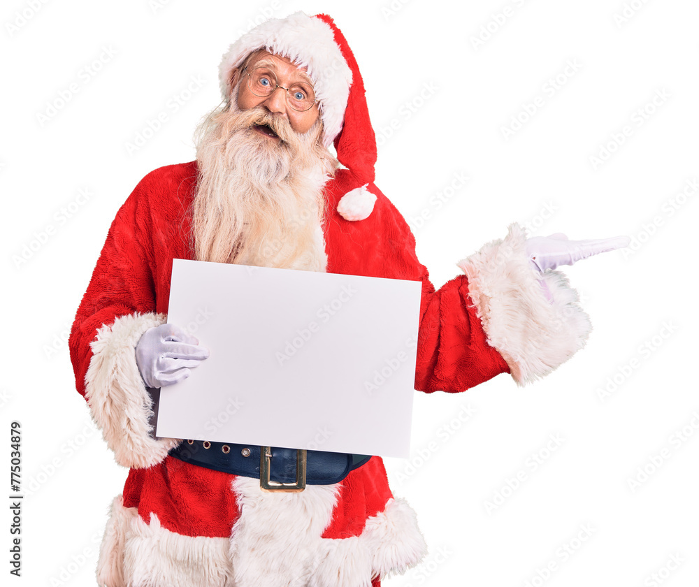 Naklejka premium Old senior man with grey hair and long beard wearing santa claus costume holding banner celebrating victory with happy smile and winner expression with raised hands