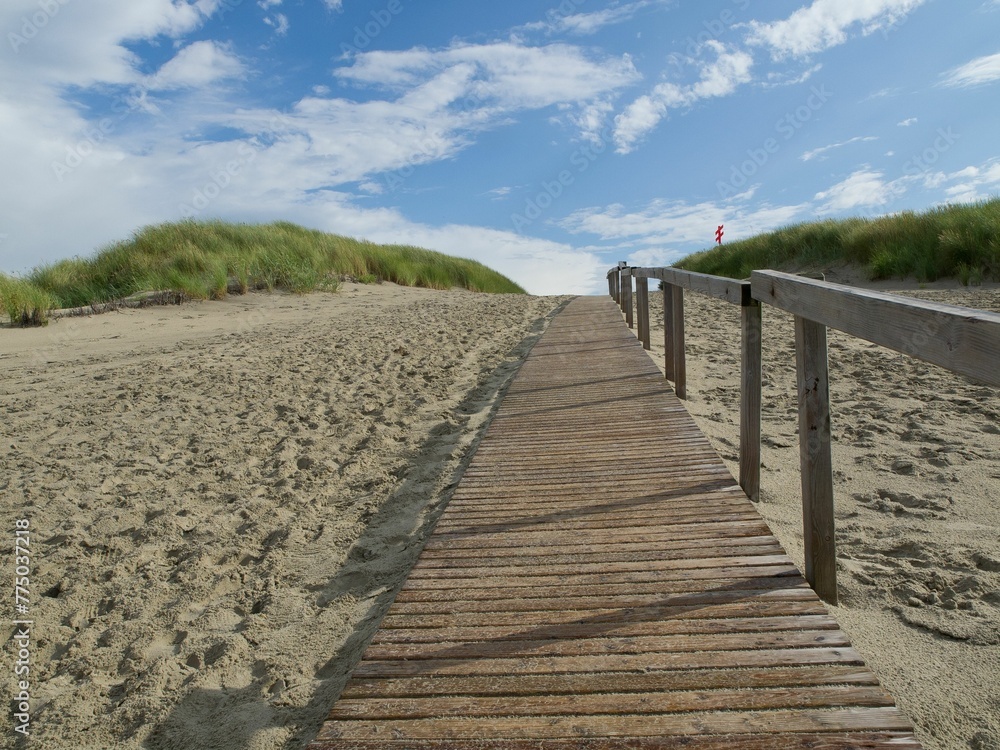 Wooden walkway in sand landscape under blue cloudy sky