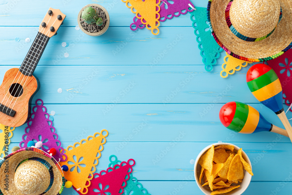 Mexican-themed arrangement for Cinco de Mayo. Overhead shot displaying cultural items: sombreros, vihuela, maracas, cactus, flag garlands, and nachos on blue wooden surface. Ideal for event promotions - obrazy, fototapety, plakaty 