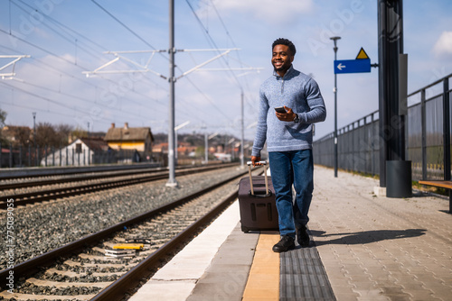 Happy man with a suitcase using phone while walking on the railway station. 