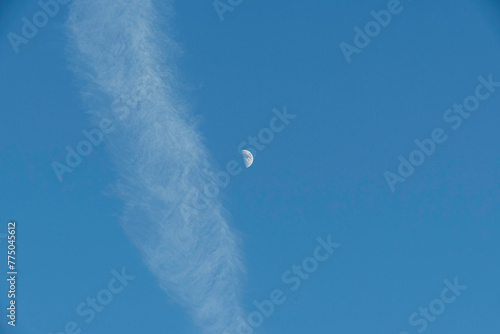 Halbmond neben weißem Wolkenband im blauen Himmel