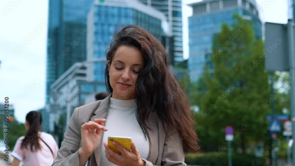 Young businesswoman texting on smartphone, touching her hair, standing outdoor Young businesswoman texting on smartphone, touching her hair, standing outdoor