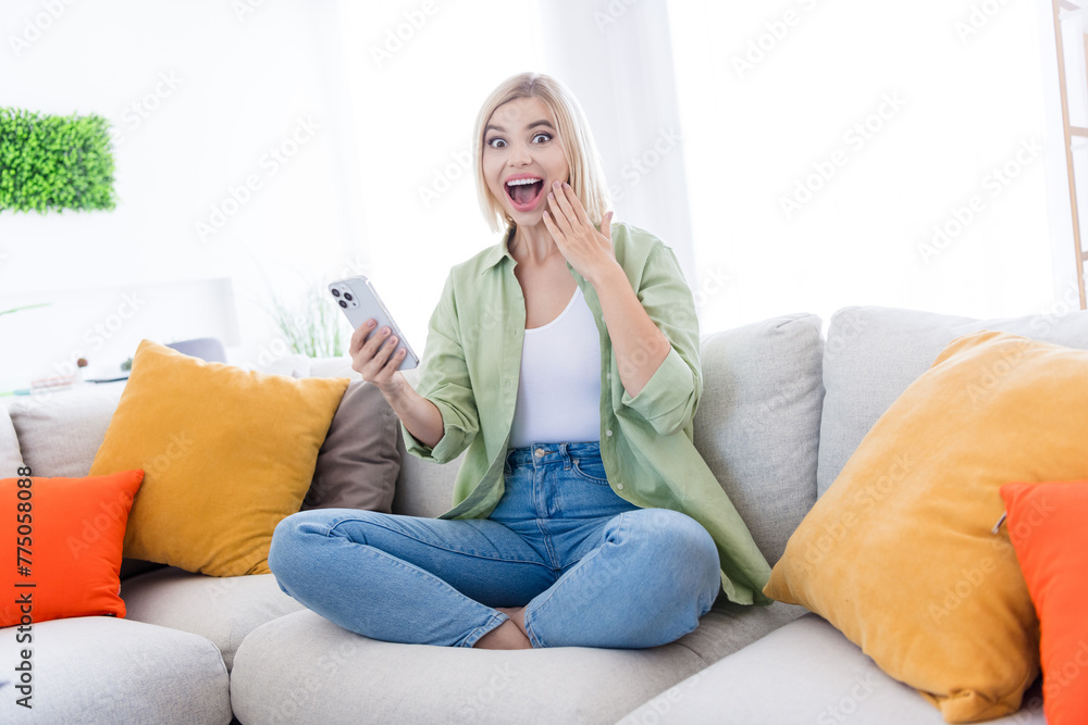 Full body size photo of sitting on divan housewife touching cheek when realize her boyfriend invite for vacation abroad indoors living room Full body size photo of sitting on divan housewife touching cheek when realize her boyfriend invite for vacation abroad indoors living room