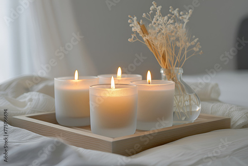 Close-up of a group of scented candles in frosted glass jars on a light wooden tray against an ivory background. 