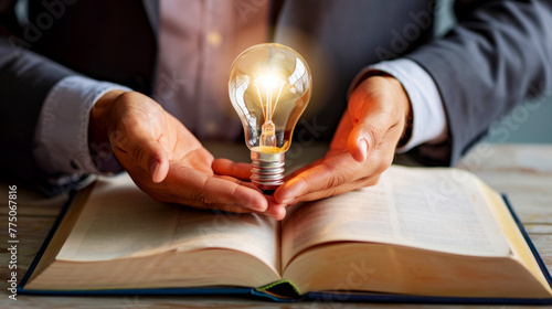 Close-up of a business executive holding an illuminated light bulb over an open book, symbolizing ideas and learning