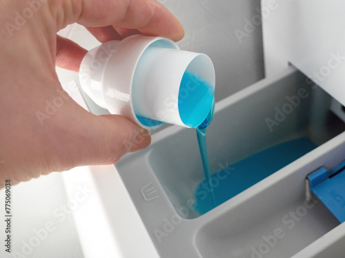 A woman pours laundry gel or conditioner into the plastic compartment of the washing machine. Laundry service