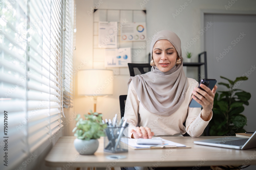 Happy Muslim businesswoman wearing hijab at work Use your laptop and smartphone to work on finance and marketing in the office. Happy Muslim businesswoman wearing hijab at work Use your laptop and smartphone to work on finance and marketing in the office.