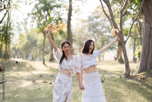 Two young friends walk together in a beautiful public place, admiring nature and holding colorful flowers.