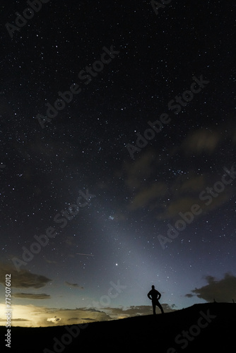A stargazer looking into the night sky silhuette showing the zodiacal light in the sky.