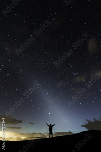 A stargazer having his hands open wide under the night sky in the middle silhuette showing the zodiacal light in the sky.