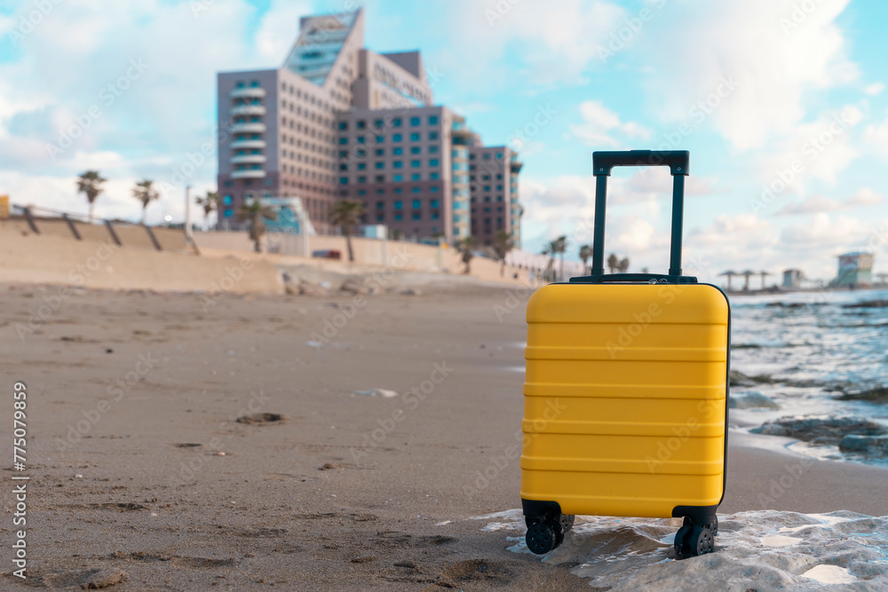 Yellow Suitcase with an orange scarf on the seaside against the sea and hotel. Travel concept.