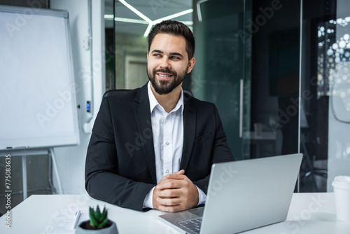 portrait of a happy bearded handsome man at workplace at computer desk in office. Business male employee entrepreneur or manager sitting at work look pensive