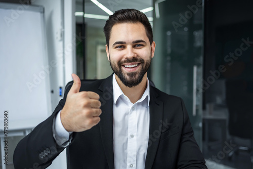 Bearded positive man looks at the camera and happily shows a thumbs up gesture.