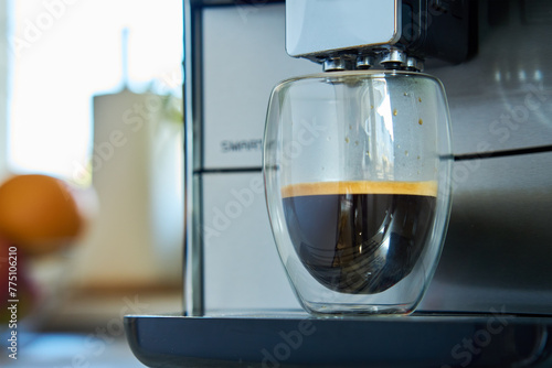 Fresh espresso in clear glass at morning. Coffee machine in kitchen  close up. Modern coffee maker with freshly brewed coffee in glass cup. Kitchen appliances
