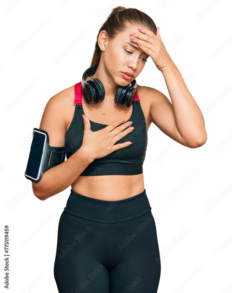 Beautiful blonde woman wearing gym clothes and using headphones touching forehead for illness and fever, flu and cold, virus sick Beautiful blonde woman wearing gym clothes and using headphones touching forehead for illness and fever, flu and cold, virus sick