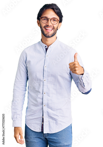 Handsome hispanic man wearing business shirt and glasses doing happy thumbs up gesture with hand. approving expression looking at the camera showing success. photo