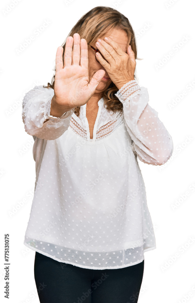 Middle age blonde woman wearing casual white shirt and glasses covering eyes with hands and doing stop gesture with sad and fear expression. embarrassed and negative concept. Middle age blonde woman wearing casual white shirt and glasses covering eyes with hands and doing stop gesture with sad and fear expression. embarrassed and negative concept.