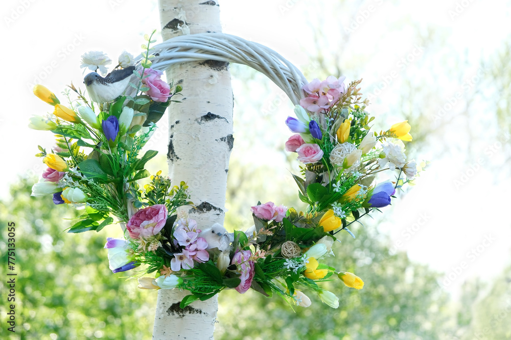 beautiful decorative Spring wreath hanging in garden, natural background. symbol of Beltane holiday. festive decor for spring - obrazy, fototapety, plakaty 