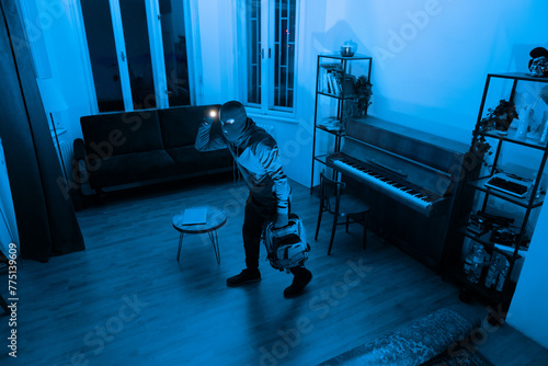 Bild auf Leinwand Burglar with mask on exploring apartment with flashlight