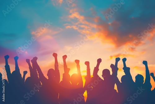 Silhouettes of people holding hands and celebrating success with arms raised against the sky at sunset, representing community 