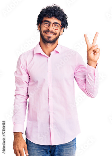 Handsome young man with curly hair and bear wearing business clothes showing and pointing up with fingers number two while smiling confident and happy.