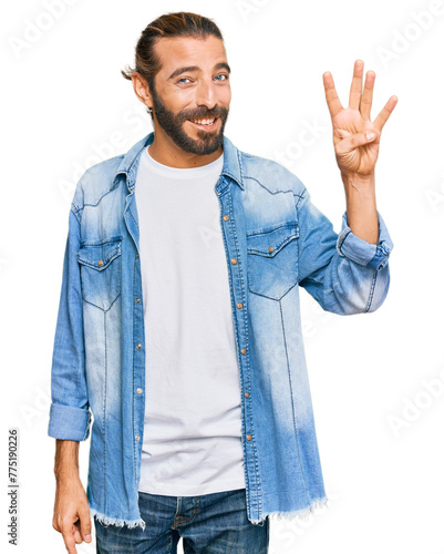Attractive man with long hair and beard wearing casual denim jacket showing and pointing up with fingers number four while smiling confident and happy.