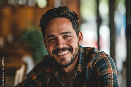 Portrait of a handsome young man with a beard smiling in a cafe. © Loli