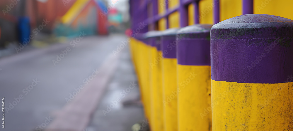 Selective focus photo capturing a row of vibrant purple and yellow bollards on an urban street with a bokeh background