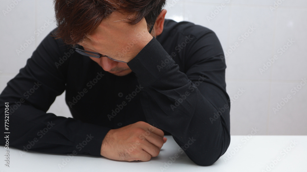 depressed young man sitting at the table and covering his face with his hands depressed young man sitting at the table and covering his face with his hands
