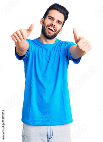 Young handsome man with beard wearing casual t-shirt approving doing positive gesture with hand, thumbs up smiling and happy for success. winner gesture.