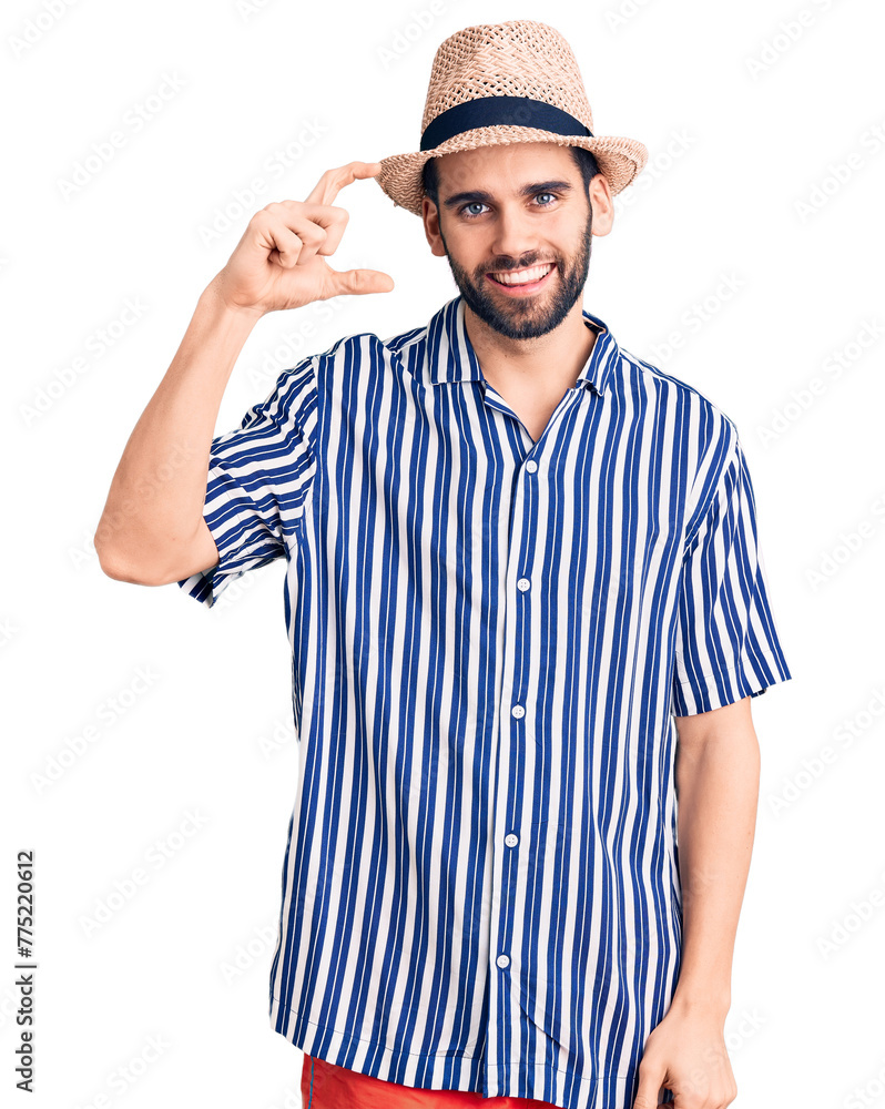 Young handsome man with beard wearing summer hat and striped shirt smiling and confident gesturing with hand doing small size sign with fingers looking and the camera. measure concept. Young handsome man with beard wearing summer hat and striped shirt smiling and confident gesturing with hand doing small size sign with fingers looking and the camera. measure concept.