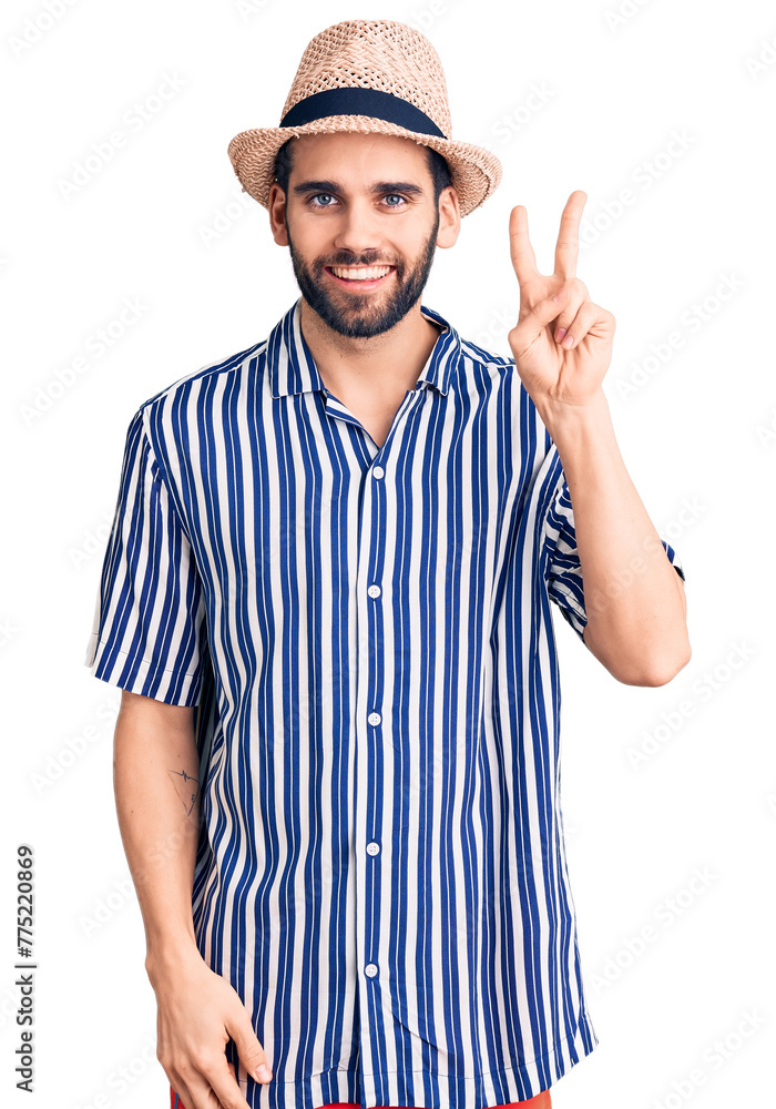 Young handsome man with beard wearing summer hat and striped shirt showing and pointing up with fingers number two while smiling confident and happy. Young handsome man with beard wearing summer hat and striped shirt showing and pointing up with fingers number two while smiling confident and happy.